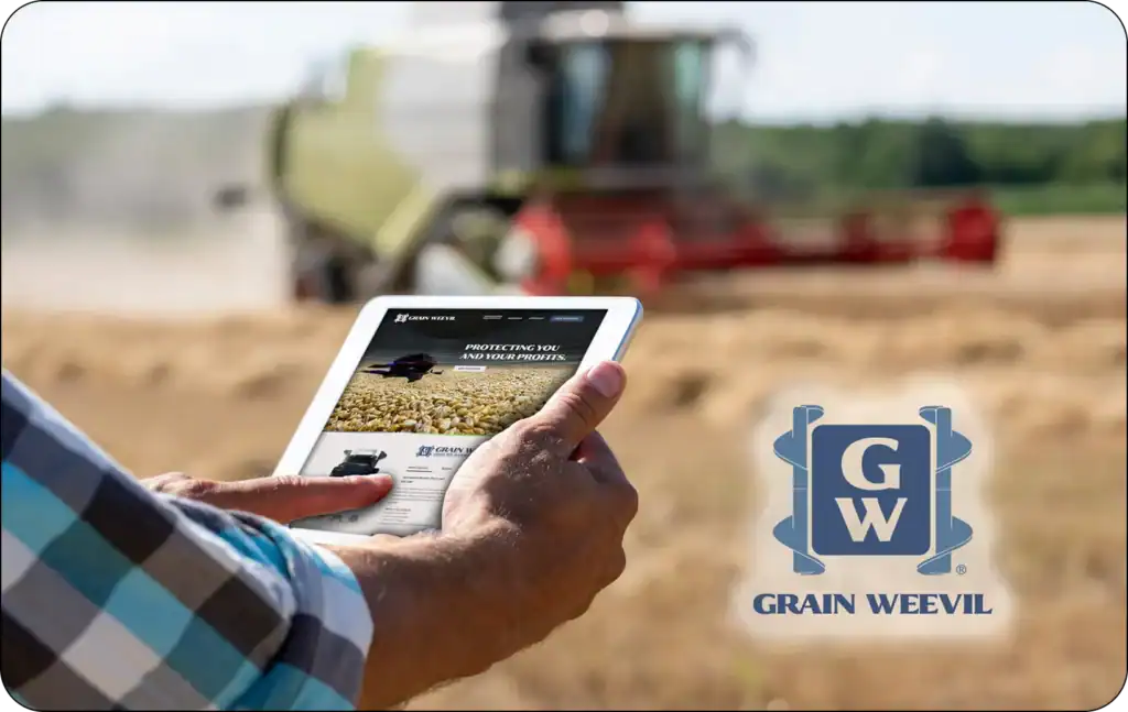 Farmer standing by a tractor in a wheat field using a tablet to view the Grain Weevil website